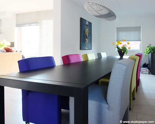 Lange zwarte eettafel met kleurrijke stoelen in moderne woonkamer