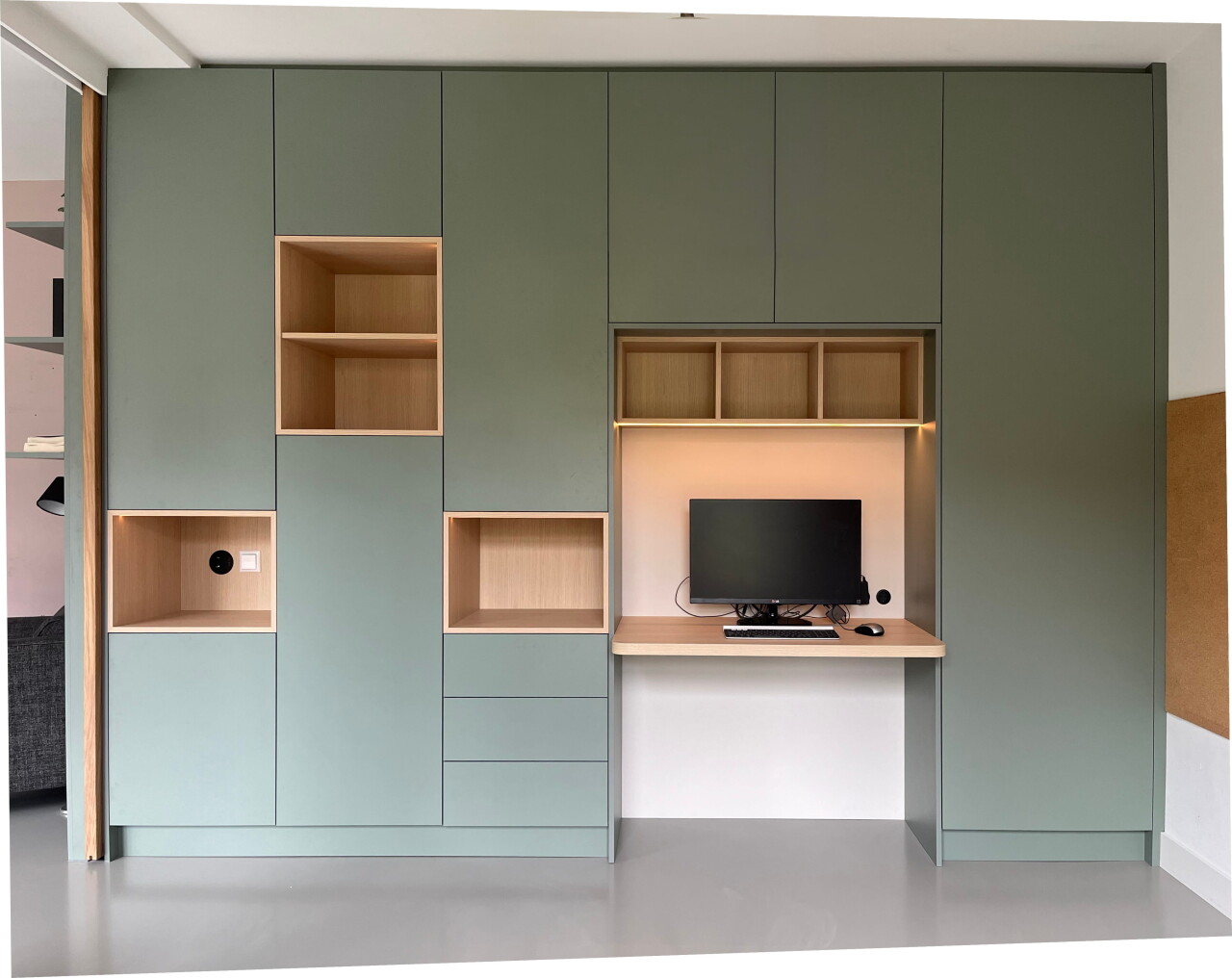 Groene maatwerk kastenwand in Castricum met groene fronten, open houten vakken en ge&iuml;ntegreerde werkplek met bureau en subtiele LED-verlichting in een rustig, modern interieur.