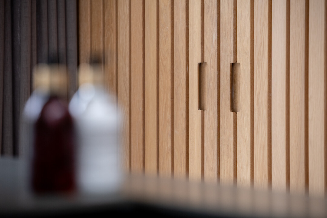 Detail van hoge keukenwand met verticale latstructuur in warm eikenhout